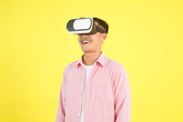 Close-up of a man wearing a VR headset, dressed in a pink shirt and white t-shirt, with a happy expression, standing isolated on bright yellow background