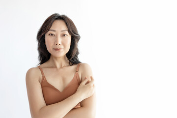 Photo of positive happy middle aged Asian lady dressed lingerie smiling arm touching shoulder empty space isolated white background. 