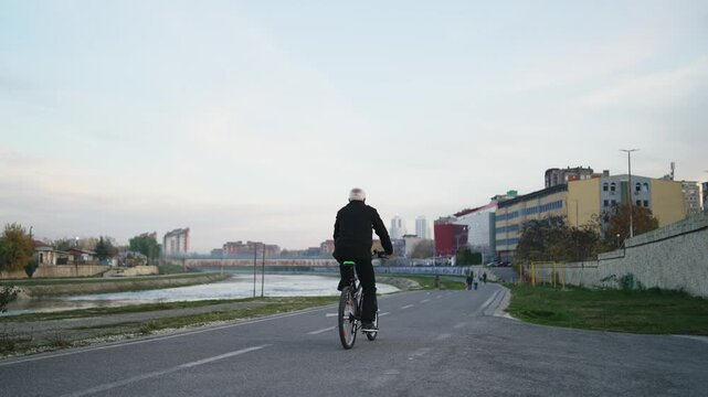 A man is riding a bicycle down a street along Vardar river in a city