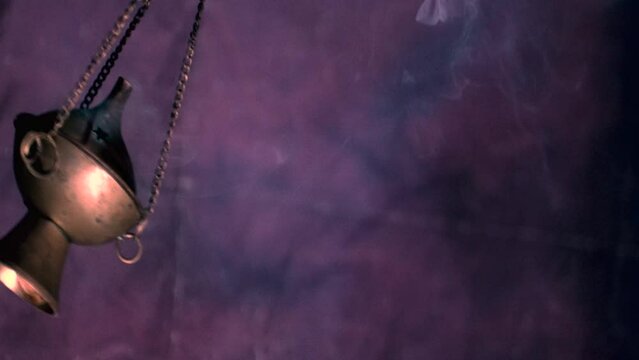 An incense burner (thurible) swinging back and fourth in slow motion, with smoke coming out of it.