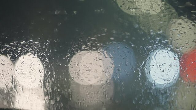 Driving on slippery road at night. Pov view from parked car windshield with rain drops and bokeh lights from moving vehicles.