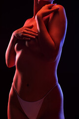 Naklejka premium Slim sexy woman in lingerie on a dark background. Her body is illuminated with blue and red lights.
