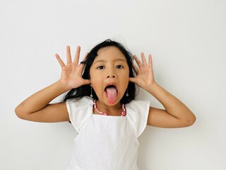 Funny Asian child girl shows tongue white background. Emotions on kid face. Happy childhood concept