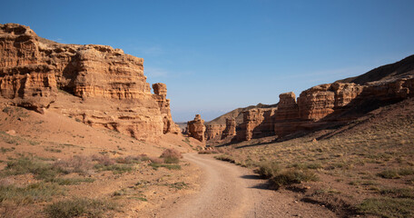 Fototapeta premium Scenic view of weathered red rock formations along a winding dirt road under a clear blue sky.