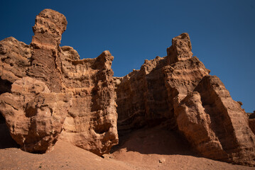Imposing red sandstone cliffs with intricate erosion patterns against a stark blue sky in a desert...