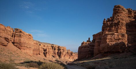 Fototapeta premium a striking formation of red sandstone cliffs set against a clear azure sky, their rugged textures highlighted by the sunlight, suggesting a peaceful desert scene in daylight