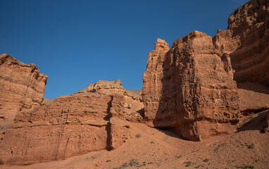 Fototapeta premium a striking formation of red sandstone cliffs set against a clear azure sky, their rugged textures highlighted by the sunlight, suggesting a peaceful desert scene in daylight