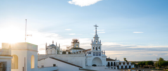 Fototapeta premium Sunlight bathes a traditional white building adorned with ornate blue tiles and a classic weather vane, set against a soft blue sky with wisps of clouds in the tranquil early morning