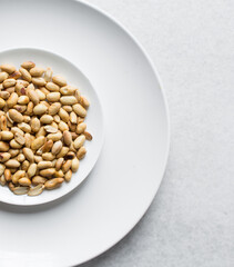 Overhead view of roasted peanuts on a white plate, flatlay of roasted peeled peanuts on a marble countertop