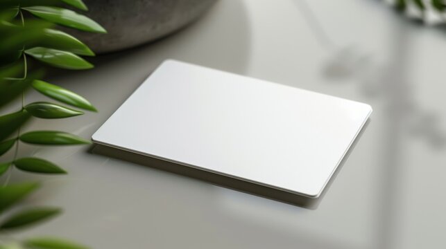 A blank white business card placed on a reflective surface with green foliage in the background, ready for customization.