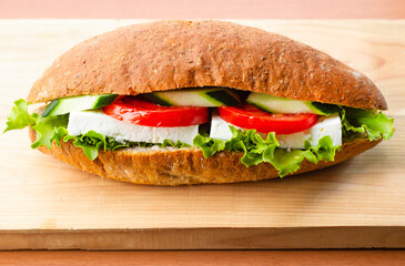 A sandwich with tomato, cucumber, feta cheese, lettuce on wooden plate