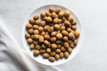 Overhead view of coated peanuts on a white plate, flatlay of cracker peanuts on a marble countertop, top view of nigerian peanut snack