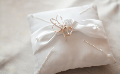 A white satin ring pillow adorned with delicate ribbons and pearls for a wedding ceremony.