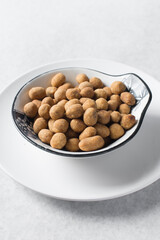 Fried coated peanuts in a white ceramic plate, cracker peanuts on a marble countertop, nigerian peanut snack in a small white plate
