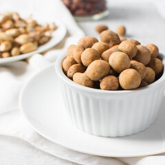 Fried coated peanuts in a white ceramic ramekin, cracker peanuts on a marble countertop, nigerian peanut snack in a small white bowl