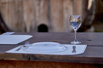 plate with empty cutlery and glass on a wooden table with a barrel in the background. Lunch at the restaurant in the courtyard of a winery.