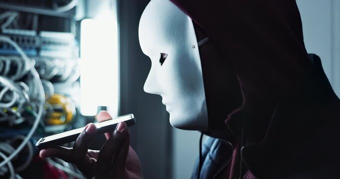 Cyber, attack and hacker in mask with smartphone in dark control room with ransomware for firewall. Phishing, crime and anonymous thief as danger to database, privacy and stealing data with malware