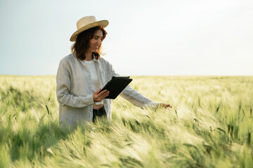 In straw hat, with tablet. Woman in white is on the agricultural wheat field