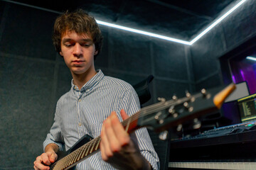 Obraz premium in the recording room equipment the sound of music a handsome young guy plays an electric guitar plucks the strings choosing the right note