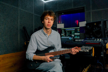 Obraz premium in the recording room equipment the sound of music handsome young guy tunes a guitar plucks the strings selecting the desired sound tonality