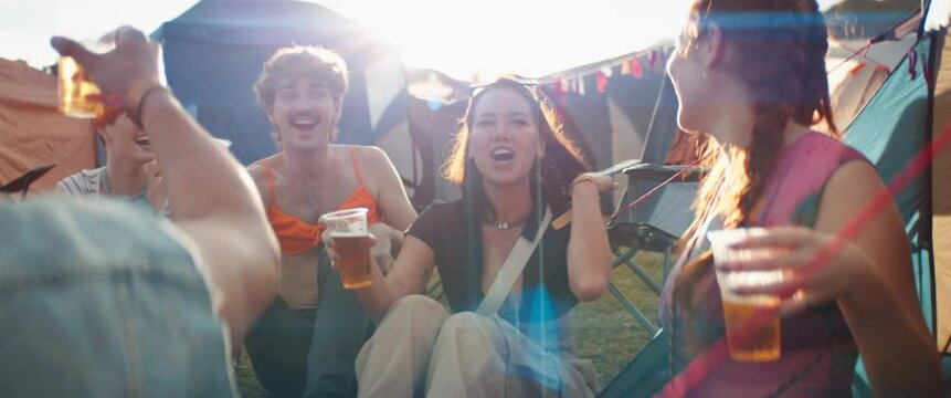 Friends having fun and laughing together at a festival campsite while enjoying a beer. Captured using an anamorphic lens and presented in the 2.39:1 CinemaScope aspect ratio.