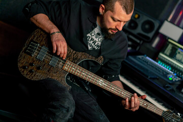 Obraz premium in the equipment of a recording room handsome man with a beard and tattoos plays an electric guitar plucks the strings choosing the right note