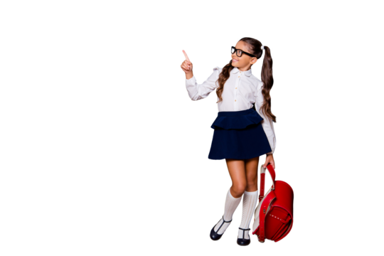 Full size body length of glad girlish dreamy nice smart cute small little girl with curly ponytails in white blouse shirt and blue skirt with red bag, pointing finger up. Isolated on black background