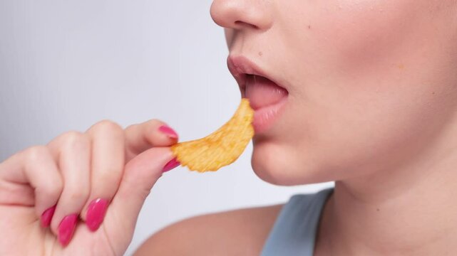 A young girl with beautiful makeup in a blue sweater eats potato chips. The concept of fast, unhealthy food.