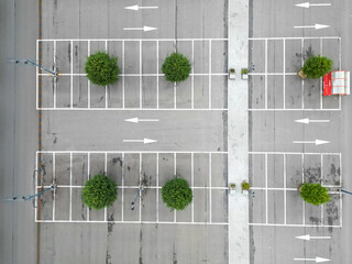 Aerial photo showing a neat, empty parking lot with white lines, green trees, and directional arrows. © Bjorn B