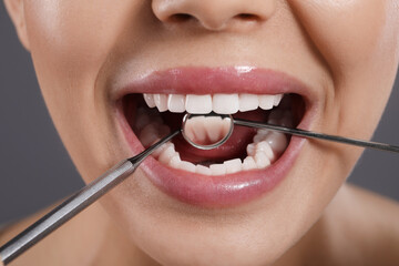 Obraz premium Examining woman's teeth with dentist's mirror on grey background, closeup