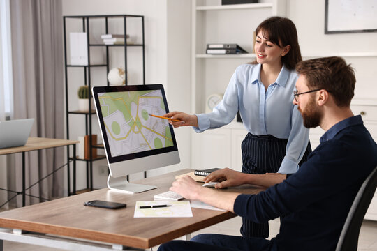 Cartographers working with cadastral map on computer at table in office