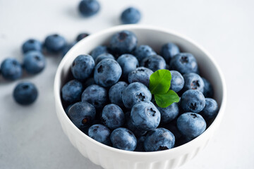 A white bowl with organic blueberries topped with a green leaf