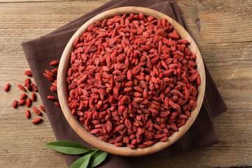 Dried goji berries in bowl and leaves on wooden table, flat lay