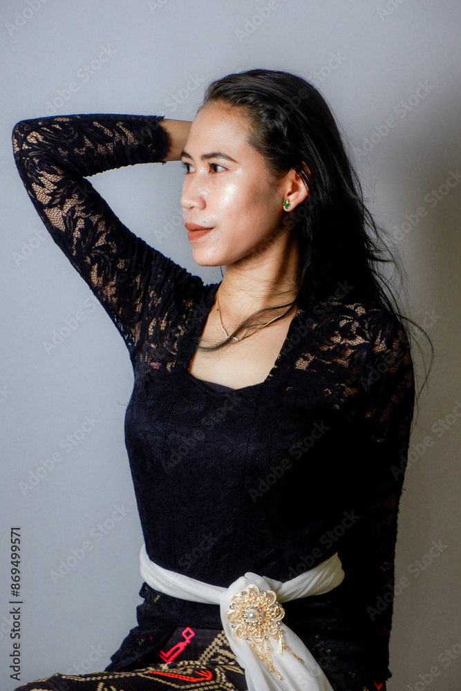 Wall mural portrait of an Indonesian woman wearing a black kebaya in the studio with a disheveled pose isolated white background