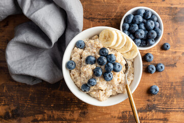 Healthy oatmeal bowl with blueberries and banana slices on a wooden table, top view