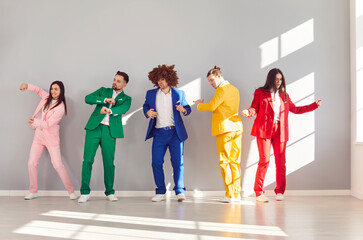 Lively group of people in colorful business suits dancing enthusiastically against a gray wall....