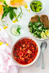Red soup with beet, beans and vegetables and cauliflower, chickpea cutlets and mixed salad with avocado, delicious hearty breakfasts or lunches, a set table with food and a vase of flowers
