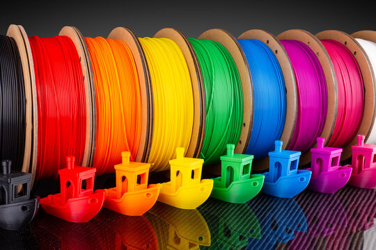 row of colorful  3d printing filament PLA material on environmentally friendly and recyclable paper cardboard spools black carbon fiber  background. modern FDM printer technology concept