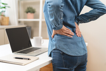 Close-up woman massaging her lower back has back pain because of sitting posture during work in office.