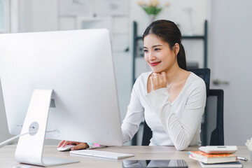 Smiling woman working on desktop while sitting in comfortable home office with notebook and documents.