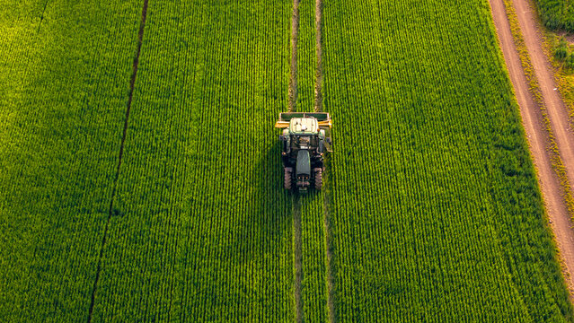  Aerial shot farmer rides a tractor with an organic fertilizer spreader to increase productivity and fertilize his fields.