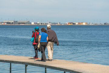 Menschen gehen auf einem Steeg, im Hintergrund der Hafen und das Meer