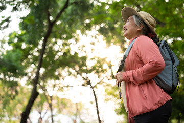Portrait of Asian mature woman in a hat with backpack behind her back, an Asia active senior woman enjoying nature in autumn park. Standing on a trail in a forest outdoors. Enjoying active travel trip