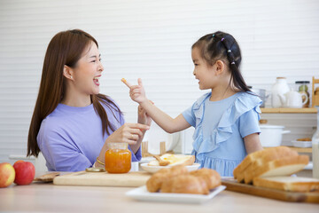 mother tasting orange jam with her daughter in the kitchen