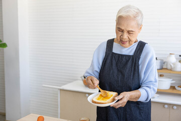 senior housewife putting orange jam on bread toast in the kitchen