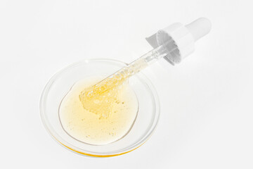 Cosmetic yellow liquid and pipette on round glass on light background