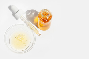Cosmetic yellow liquid, jar and pipette on round glass on light background