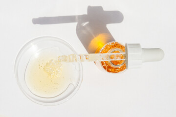 Cosmetic yellow liquid, jar and pipette on round glass on light background