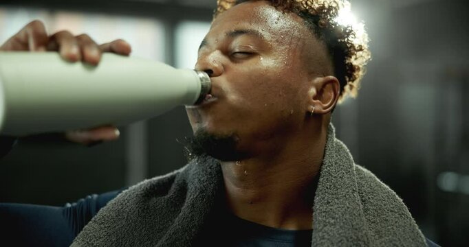 Drinking, water and black man in gym with fitness, sweat and break at workout with towel. Sports, relax and athlete with protein shake in bottle for thirst, exercise and healthy nutrition at club