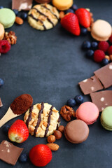 Macarons, chocolate, cookies, berries and various nuts on dark blue background. Selective focus.
